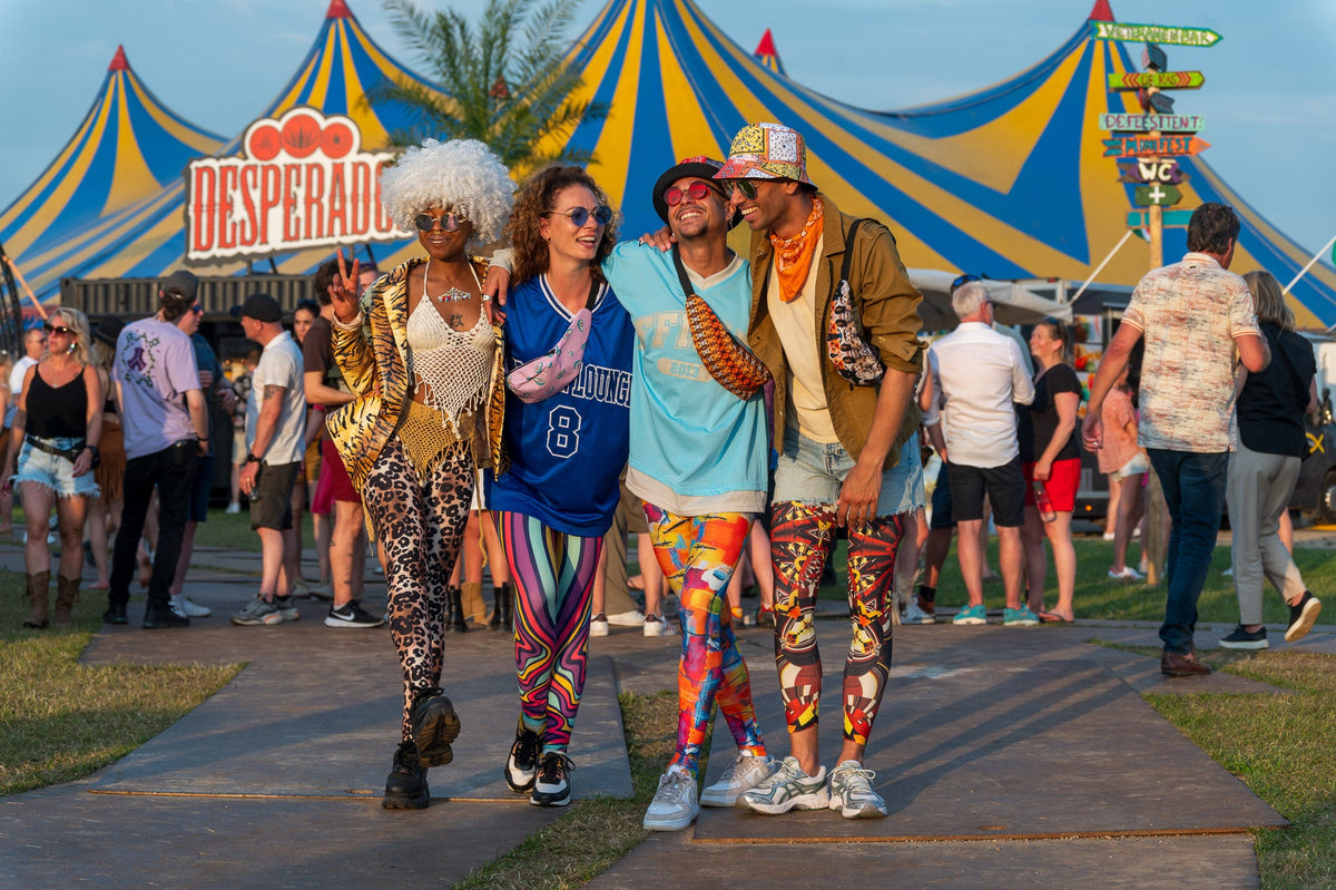 Vier vrienden in bonte printleggings, pruik en glitterjasje voor een circustent, klaar voor carnaval